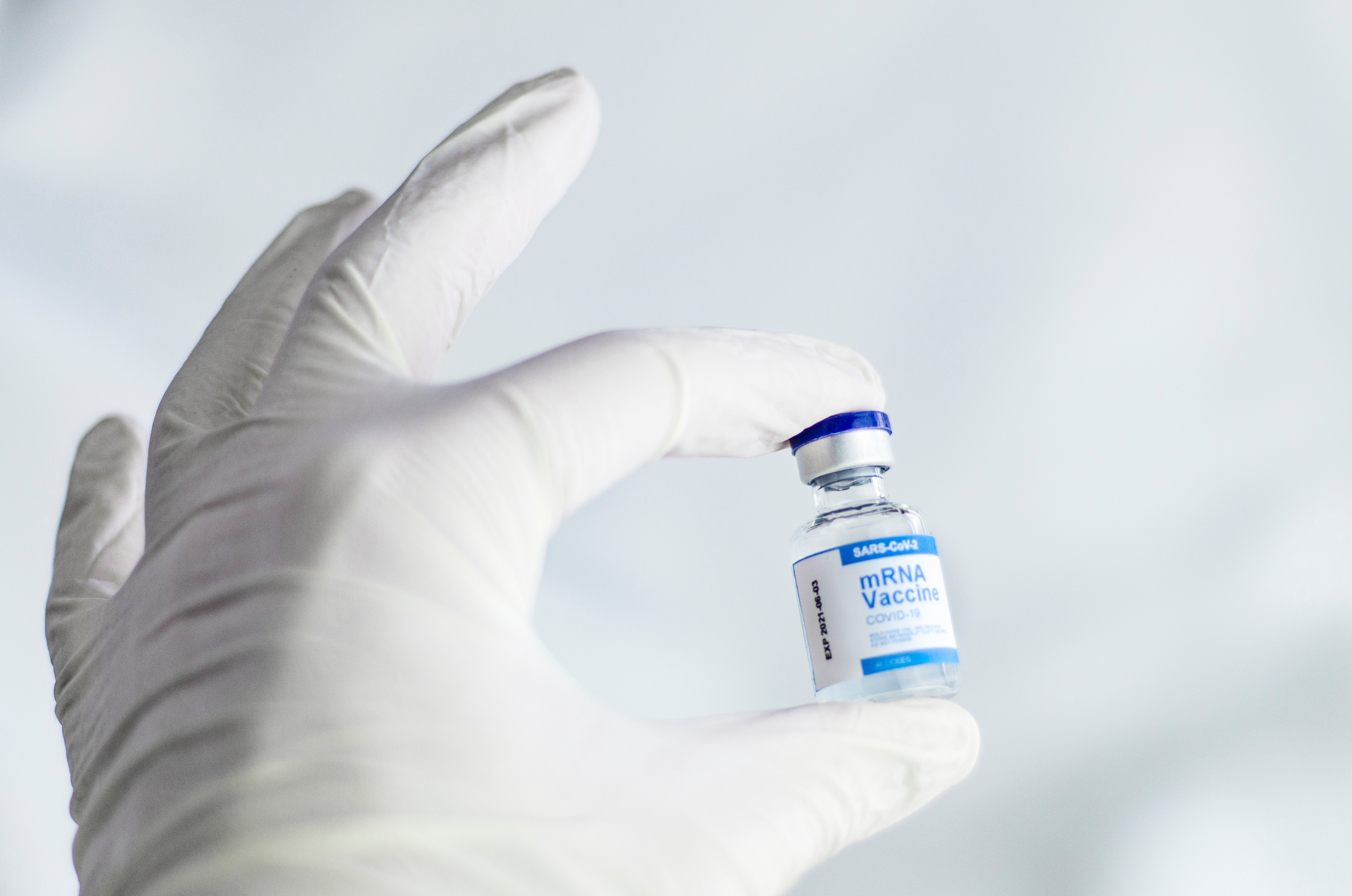 A doctor's white glove-covered hand holds a vial of the COVID mRNA vaccine.