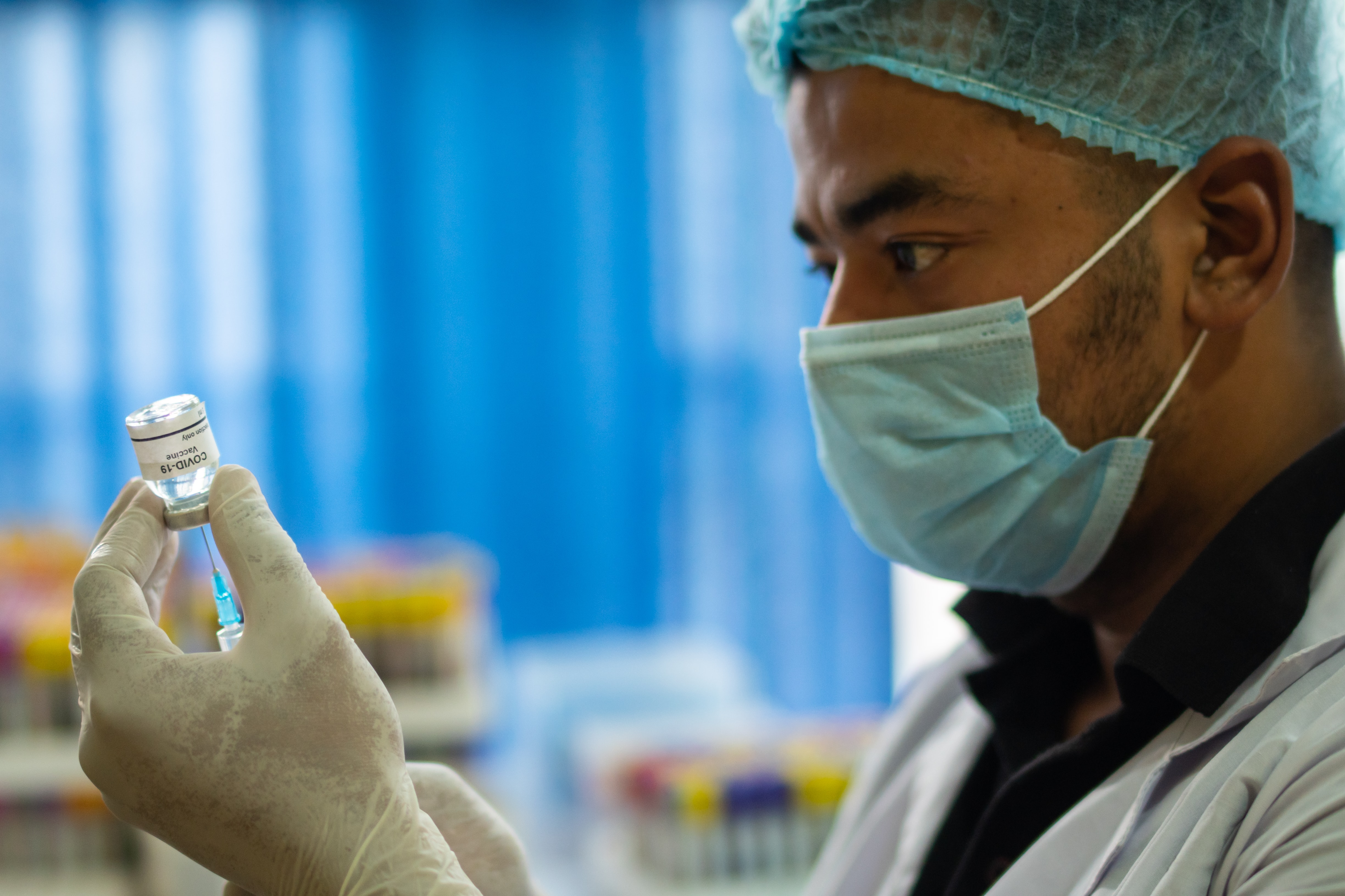 A doctor wearing a mask uses a needle to prepare a vial of COVID-19 vaccine.